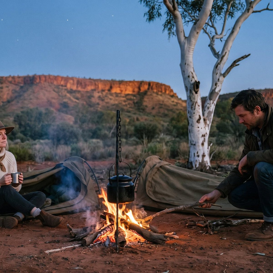 Canvas tent glowing at dusk beside a still river below red Kimberley gorge walls